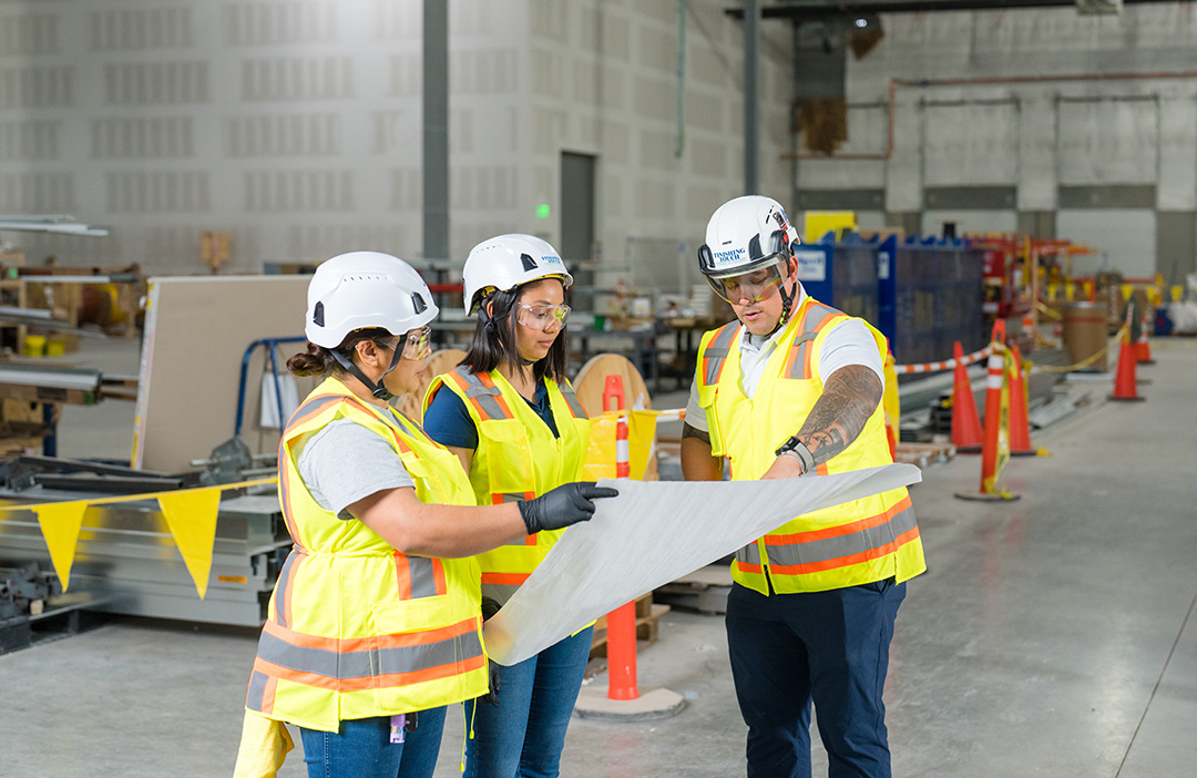 two women and one man wearing PPE equipment review floor plans in a warehouse space